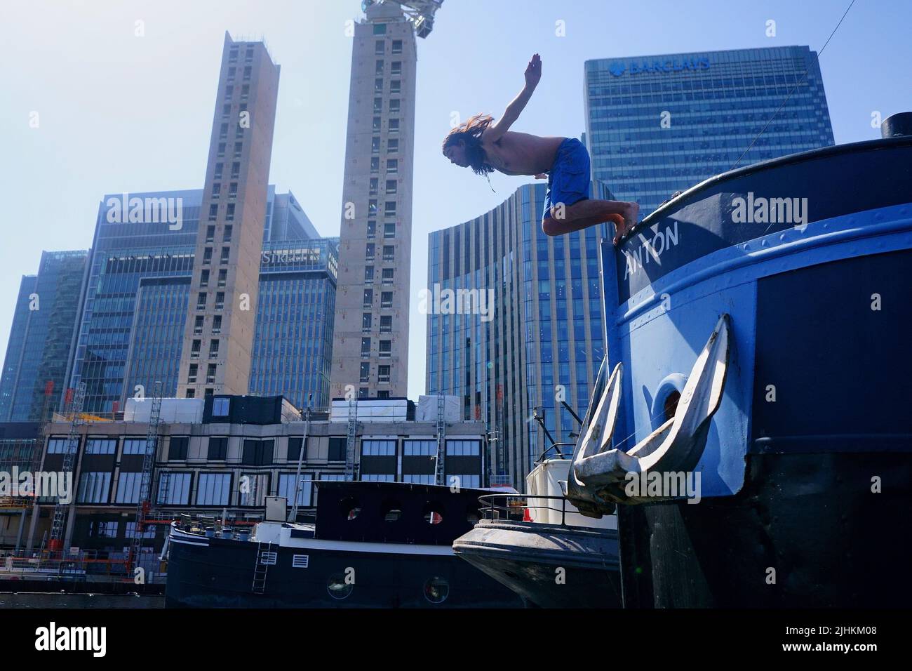 A swimmer dives from a houseboat in the Canary Wharf docklands in east London. Temperatures have reached 40C for the first time on record in the UK, with 40.2C provisionally recorded at London Heathrow, the Met Office has said. Picture date: Tuesday July 19, 2022. Stock Photo