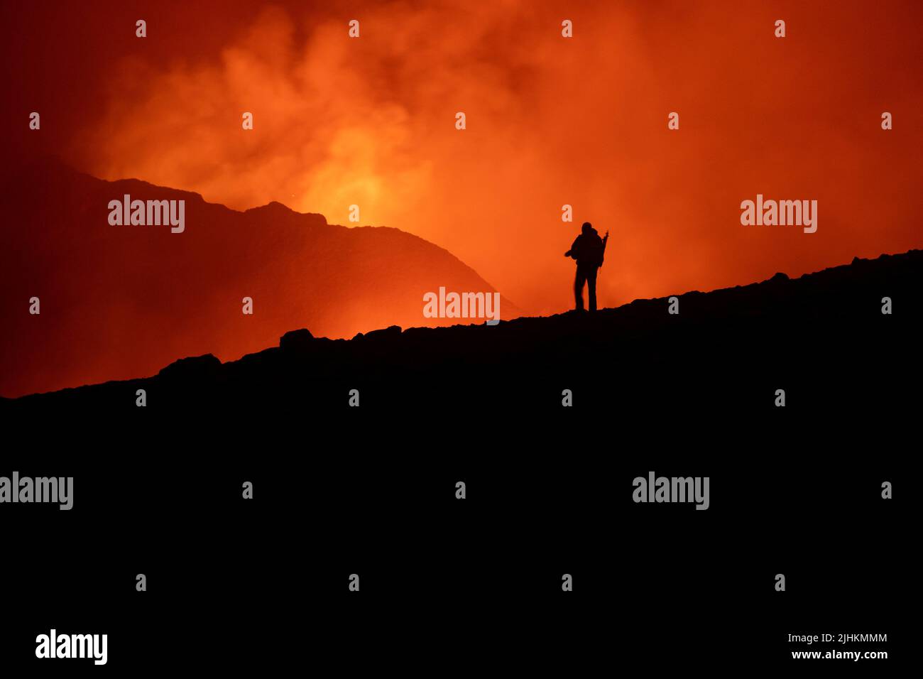 A silhouette of a tourist looking at and photographing the eruption in Iceland in 2021, the person is not identifyable and is set against the orange s Stock Photo
