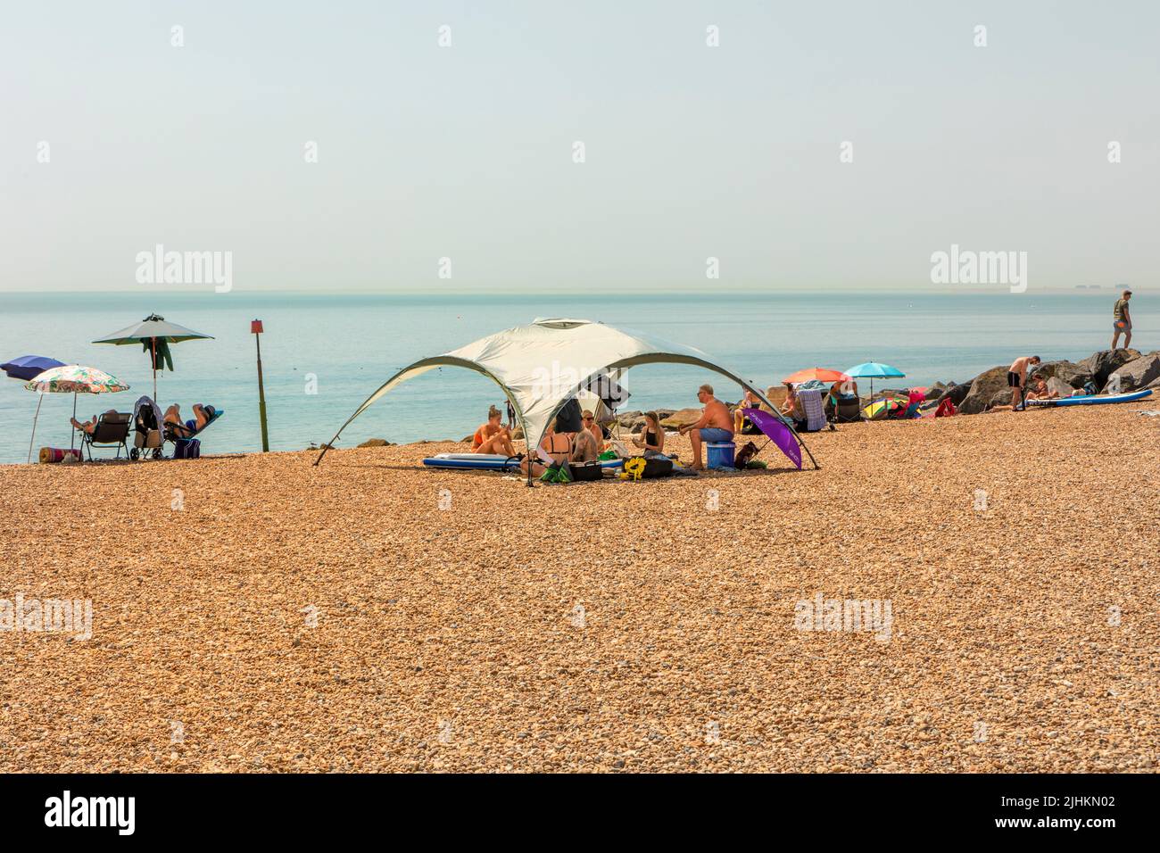 Holidaymakers under a large beach canopy on a shingle beach Stock Photo