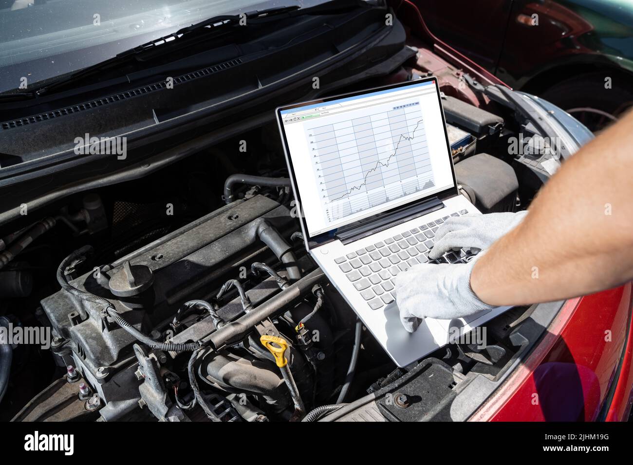 Young Male Mechanic Using Laptop While Examining Car Engine Stock Photo