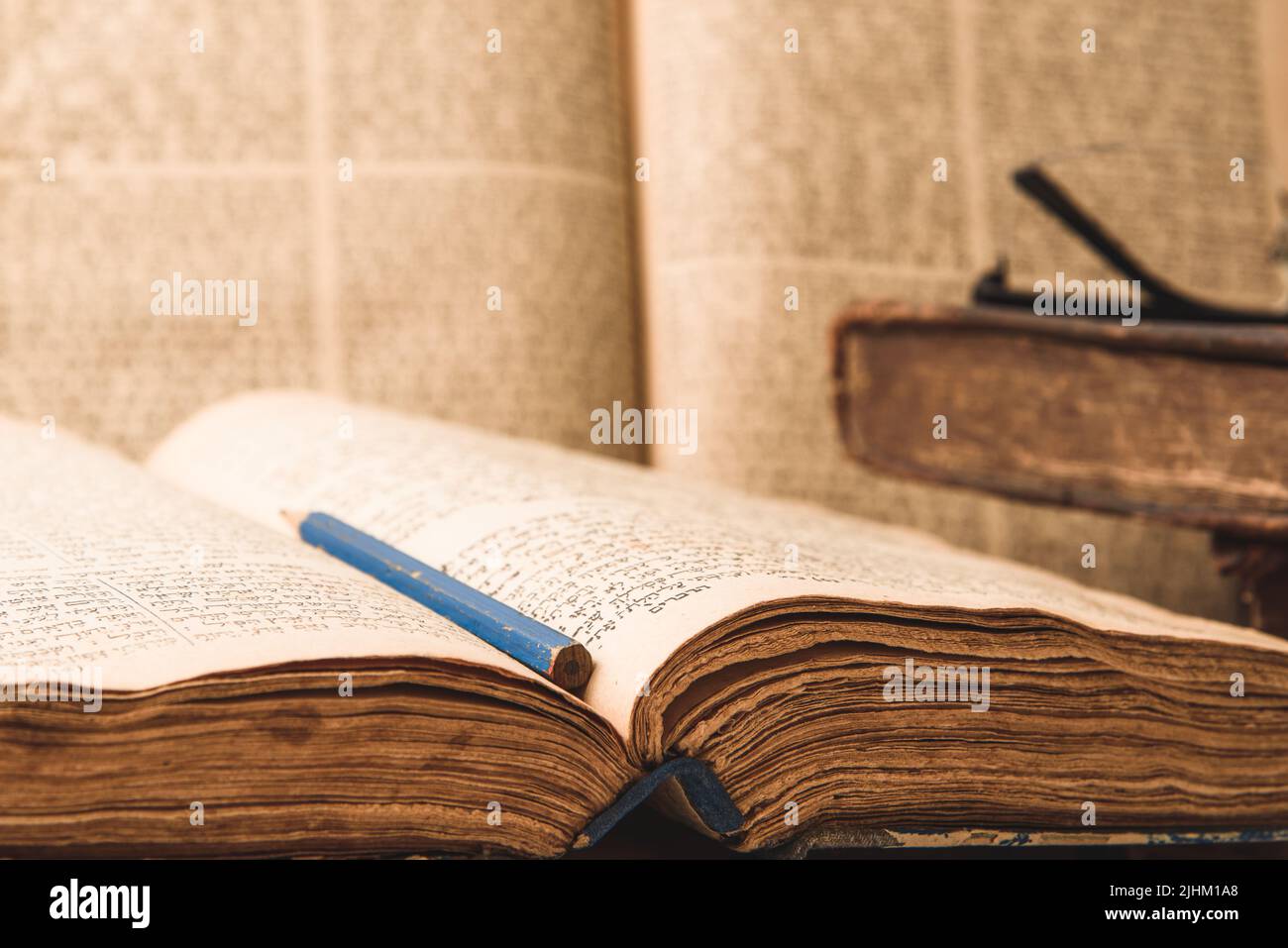 Old worn shabby jewish books in leather binding and open blurred Torah in the background. Closeup. Selective focus Stock Photo