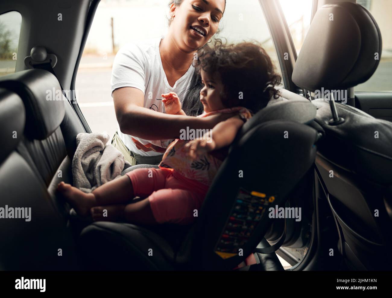Doing it all by herself. a young woman strapping her baby into her car seat. Stock Photo