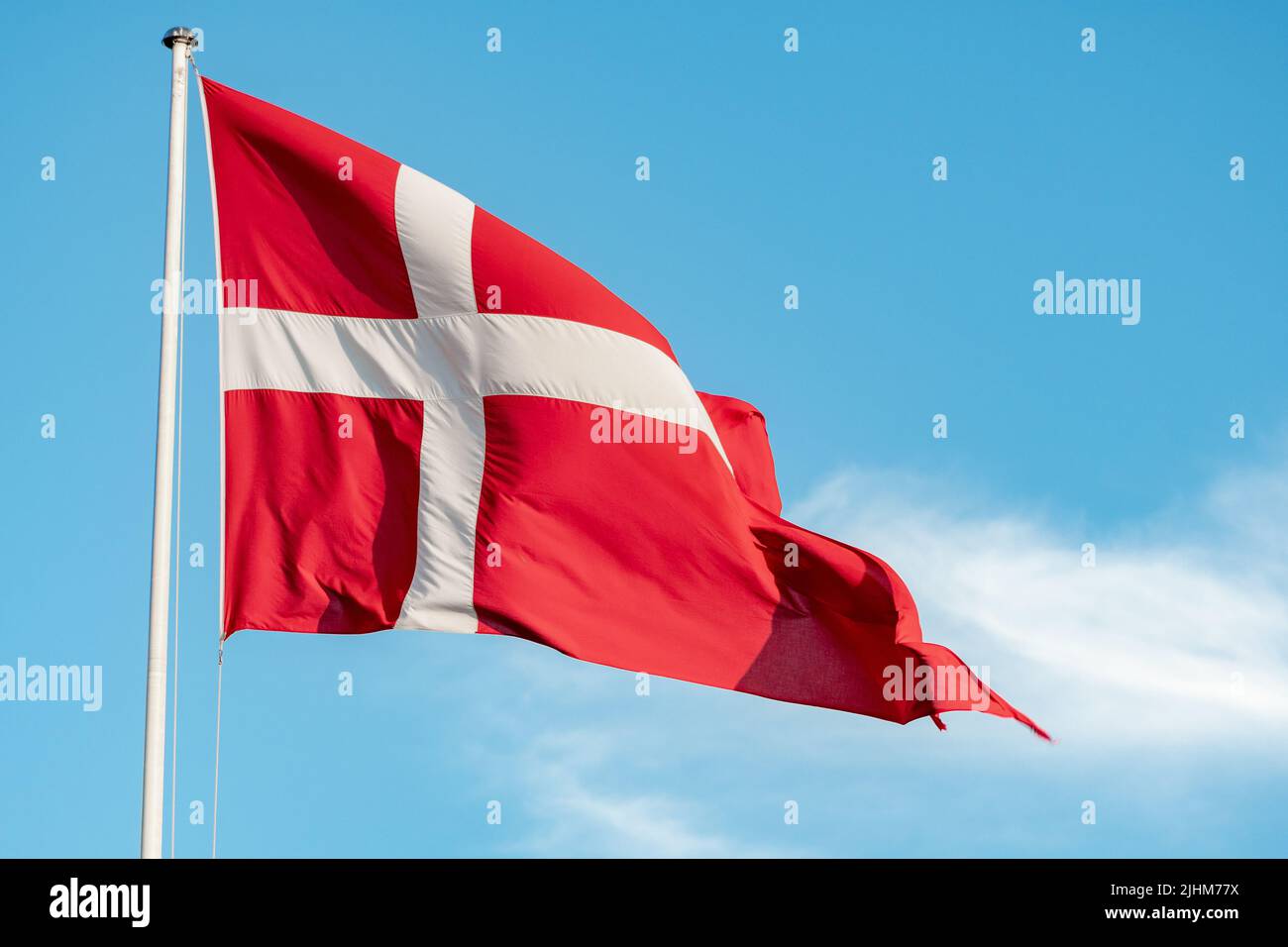 Beautiful flag of Denmark or Danish flag under the sun on a flagpole with blue sky on background, close up Stock Photo
