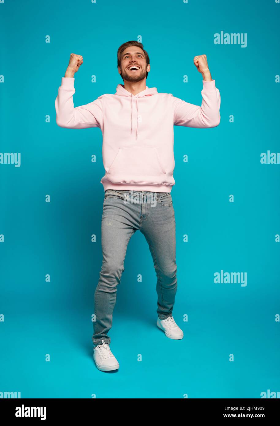 Full length of a cheerful young man standing and celebrating success isolated over light blue background Stock Photo