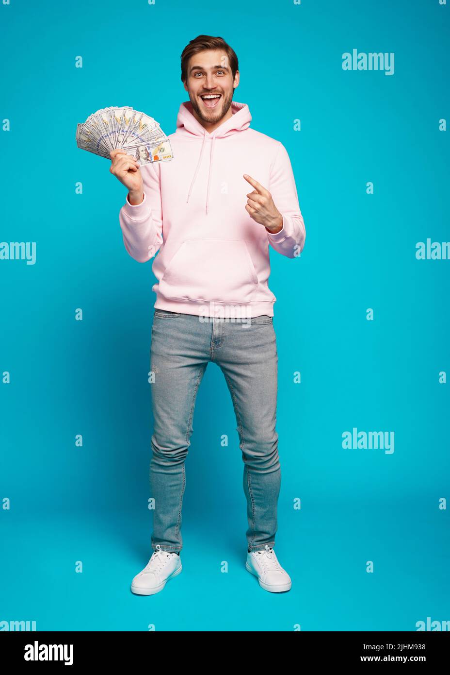 Portrait of a joyful young man holding money cash and celebrating isolated over light blue background Stock Photo