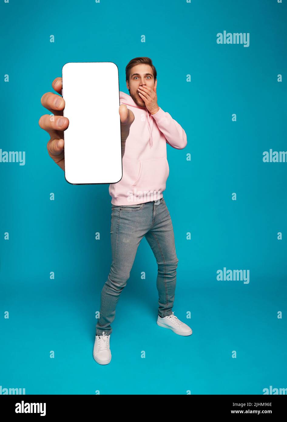 Mobile App Advertisement. Handsome Excited Man Showing Pointing At Empty Smartphone Screen Posing Over Light Blue Studio Background, Smiling To Camera Stock Photo