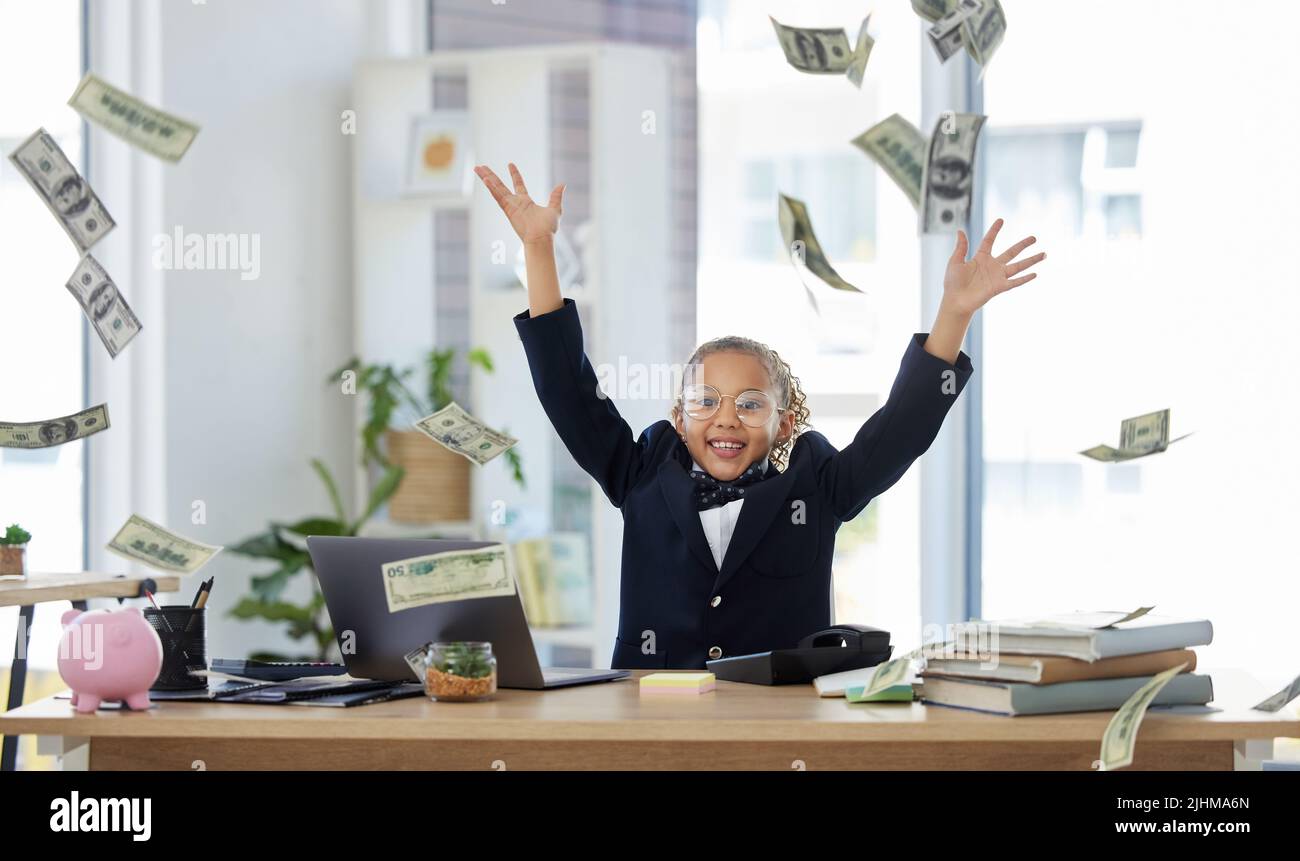 Its raining money. an adorable little girl dressed as a businessperson sitting alone in an office and throwing money. Stock Photo