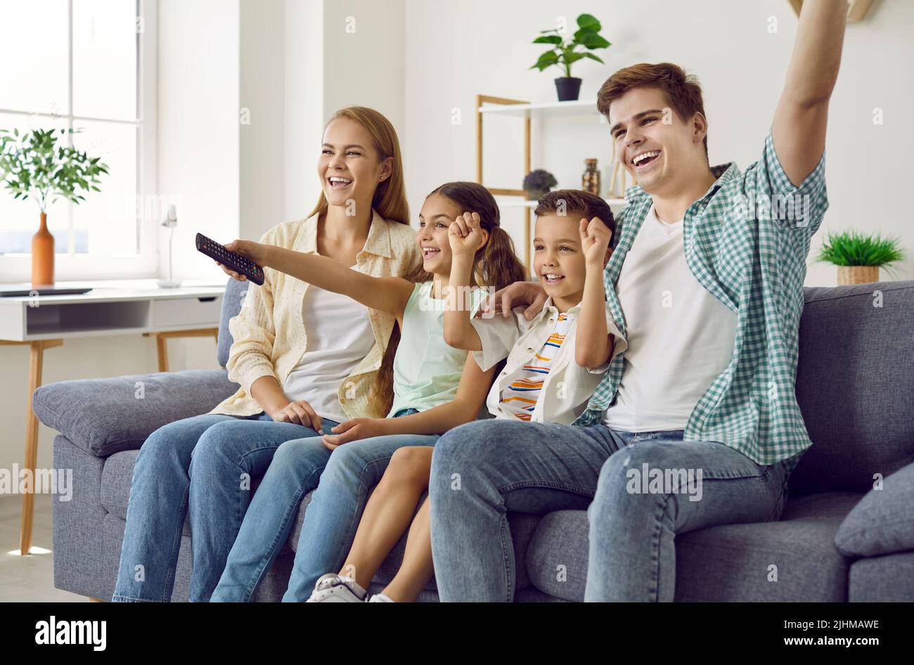 Happy mom, dad and children sitting on the sofa at home and watching television all together Stock Photo