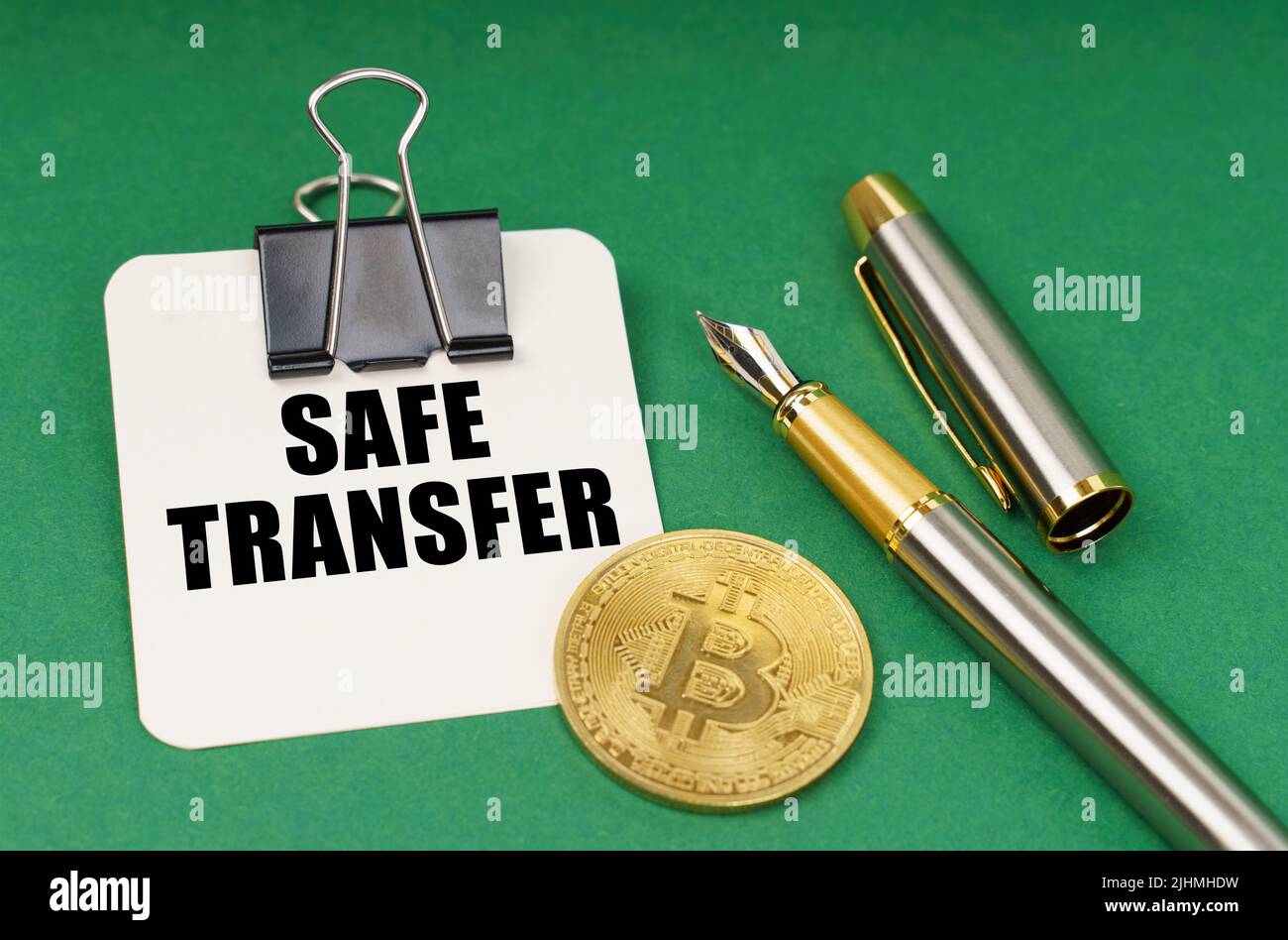 Cryptocurrency and business concept. On a green surface, a bitcoin coin, a pen and a sheet of paper with the inscription - safe transfer Stock Photo