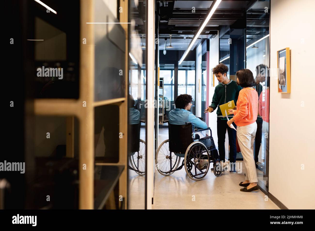 Multiracial colleagues discussing with businessman sitting in wheelchair at office corridor Stock Photo