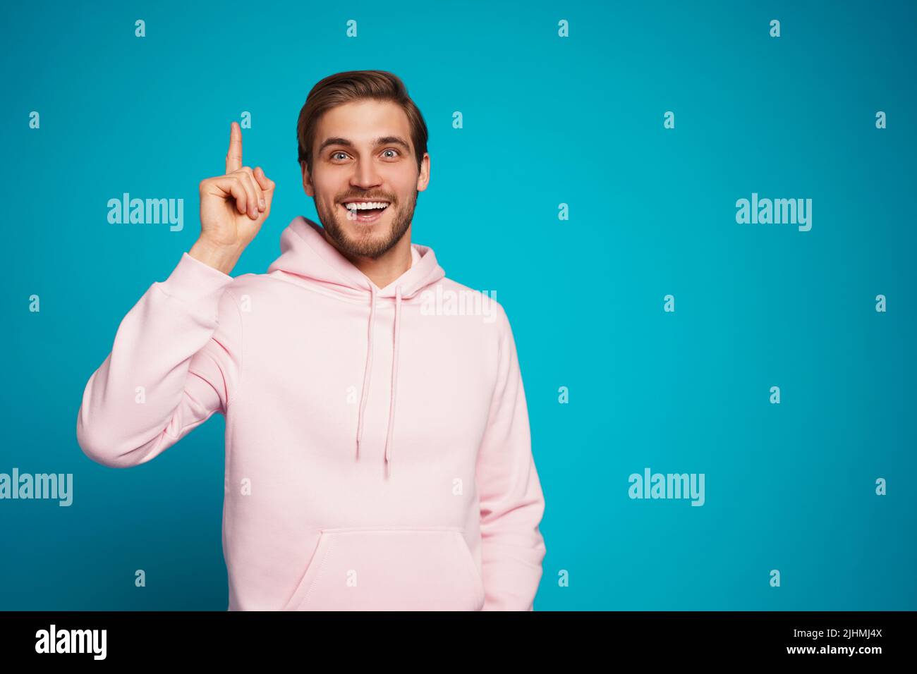 Portrait of an excited happy man pointing finger up at copyspace isolated on a light blue background. Stock Photo