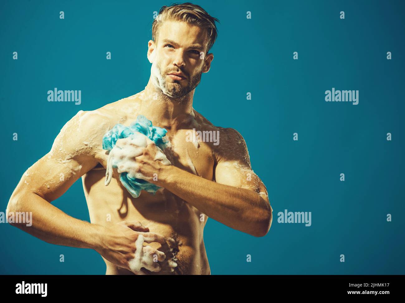 Sexy macho taking shower. Bearded hipster is washing body with sponge. Skin care, spa, beauty. Stock Photo