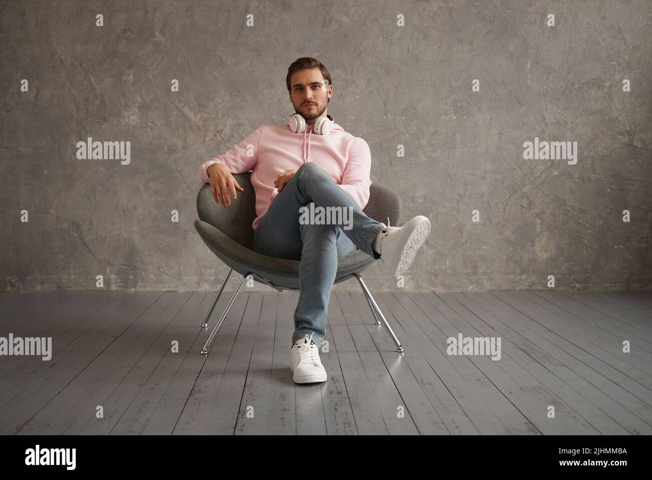 Feeling comfortable anywhere. Full length of handsome young man looking at camera while sitting against gray background Stock Photo
