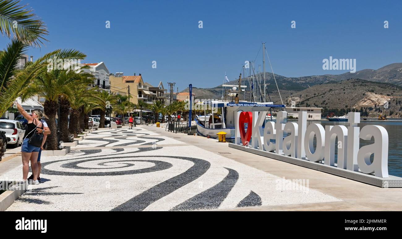 Argostili, Kefalonia, Greece - June 2022: Panoramic view of two people taking a selfie in front of a I Love Kefalonia sign on the harbour in Argostili Stock Photo