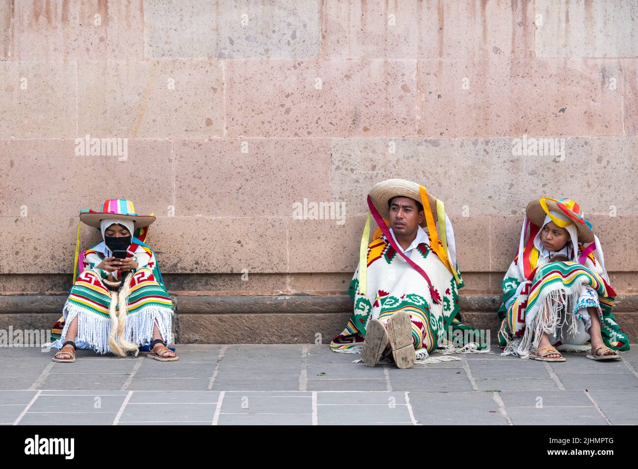 Young Mexican boys, dressed in costume, take a break from performing the Danza de los Viejitos outside the Basílica de Nuestra Señora de la Salud, or Basilica of Our Lady of Health, during celebration of the traditional Sunday service marking the start of holy week, April 10, 2022 in Patzcuaro, Michoacan, Mexico. Stock Photo