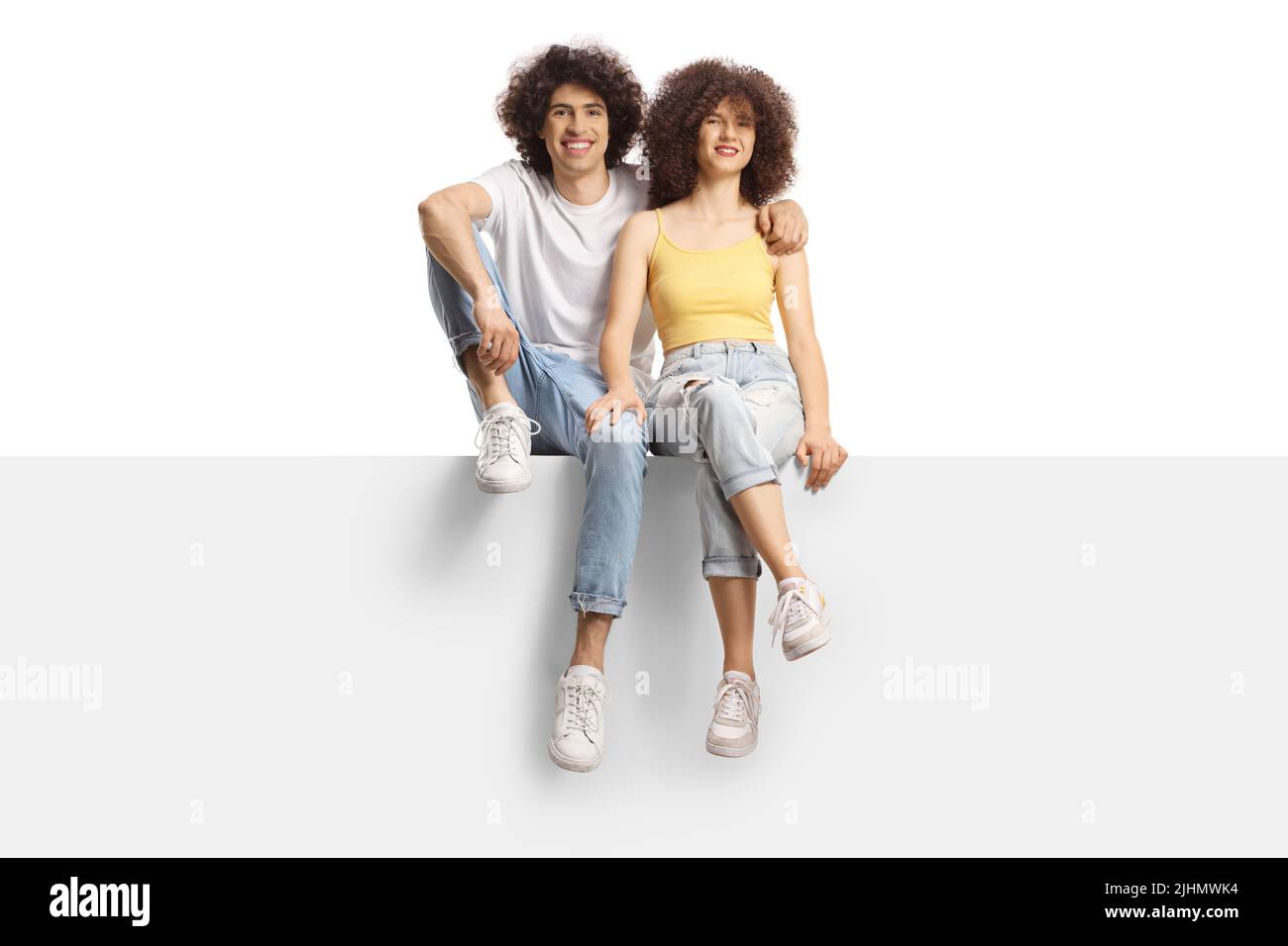 Young man and woman with curly hair smiling sitting on a blank panel isolated on white background Stock Photo