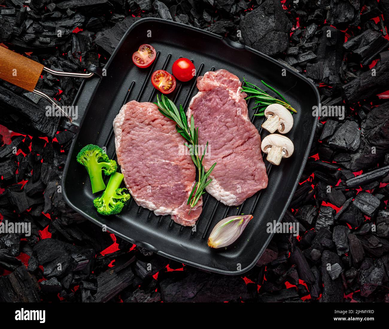 Raw steak with vegetables and herbs on a grill pan. On burning charcoal barbeque. Organic meat