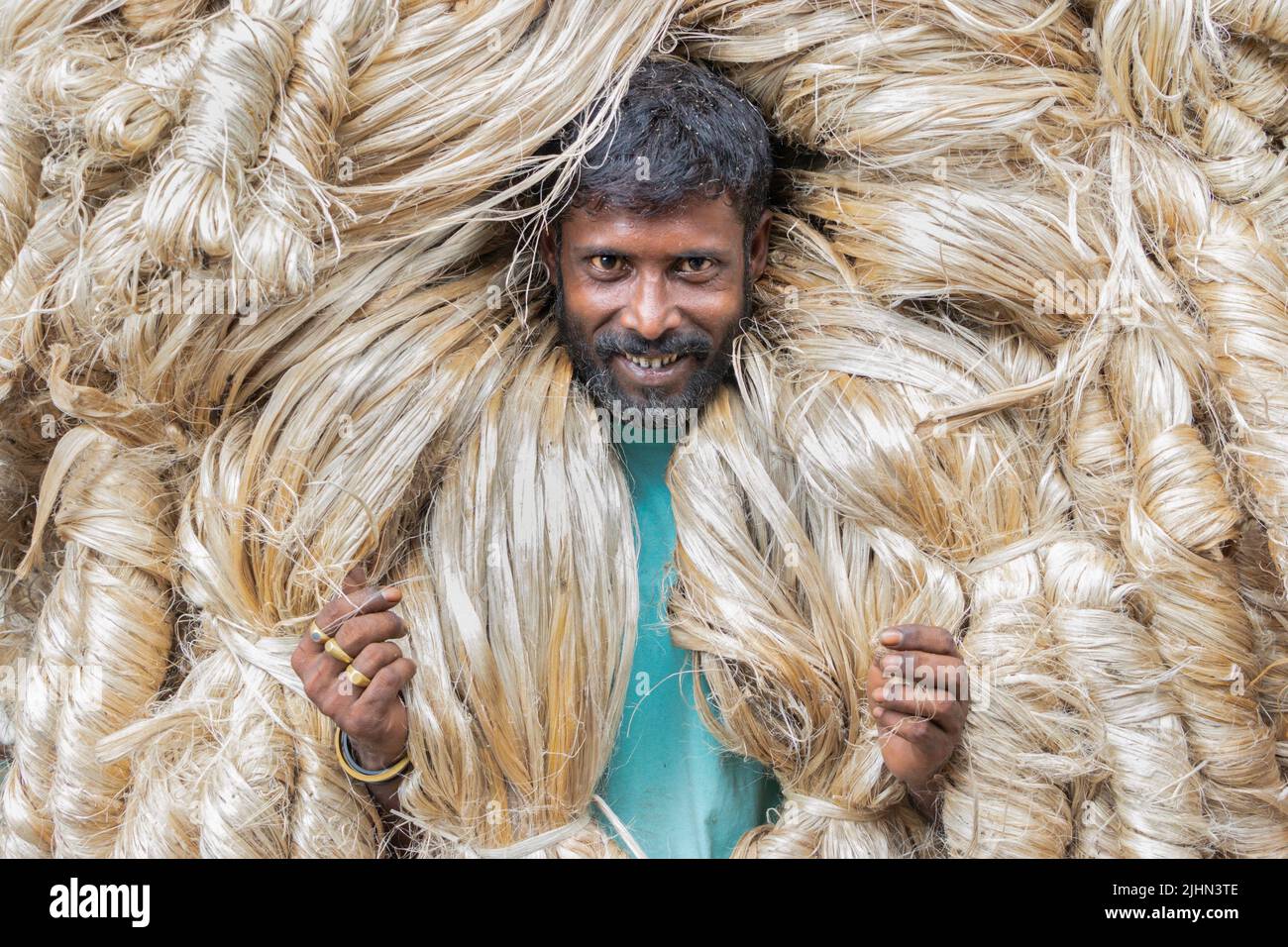 July 20, 2022, Manikganj, Dhaka, Bangladesh: Workers carry 50kg bundles of newly harvested jute above their heads to sell at a market in Manikganj, Bangladesh. The Golden Fiber of Bangladesh, Jute offers an alternative to plastic bags because of its biodegradable properties. The diligent workers appear to be wearing large golden wigs and their bodies are enveloped with the heavy natural fibers, with only their faces visible as they each carry around 50kg of jute on their shoulders. Bangladesh is the second biggest producer of jute after India and the largest exporter of jute and jute products Stock Photo