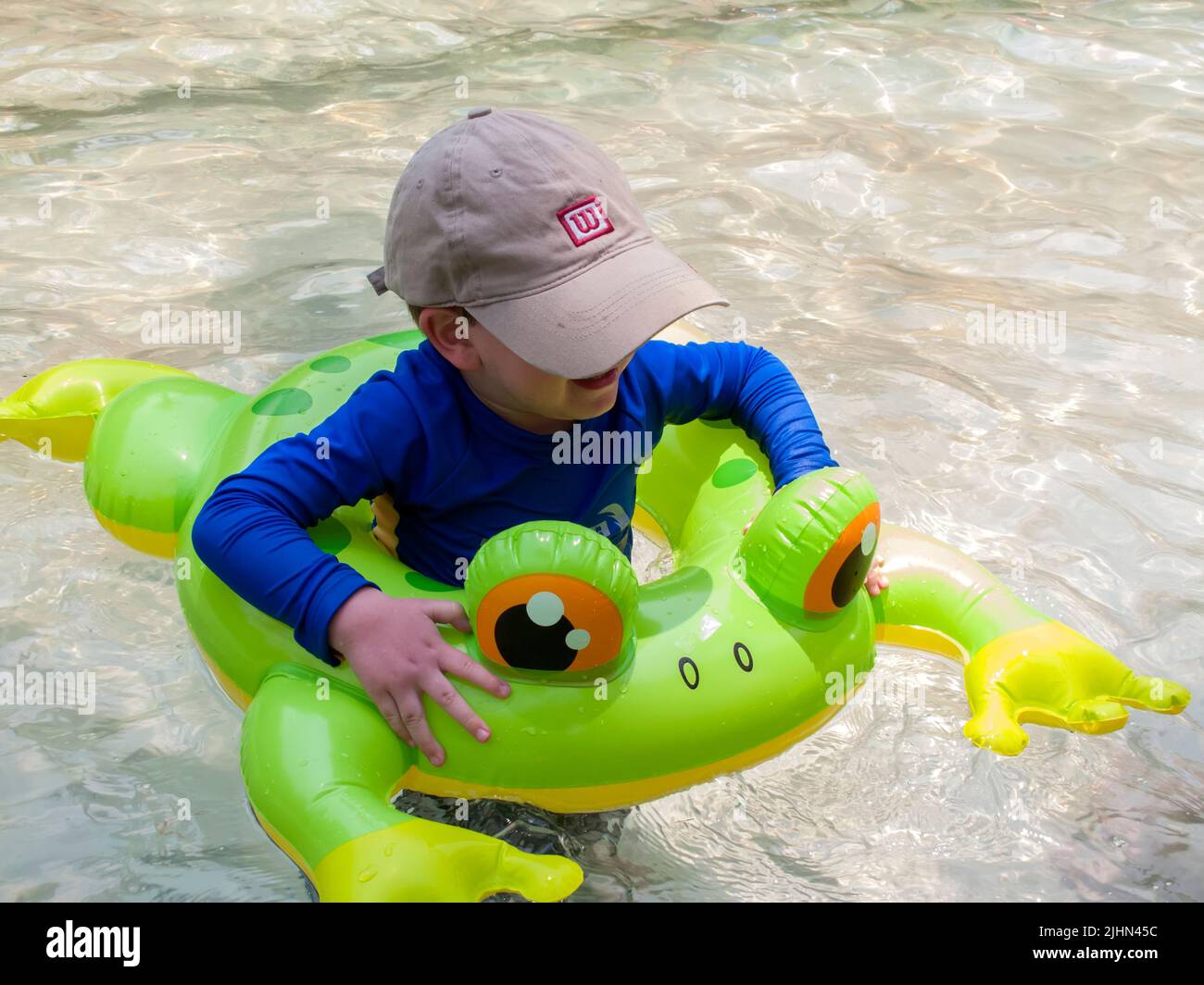 Young boy in frog floatation tube cooling off in swimming pool Stock Photo