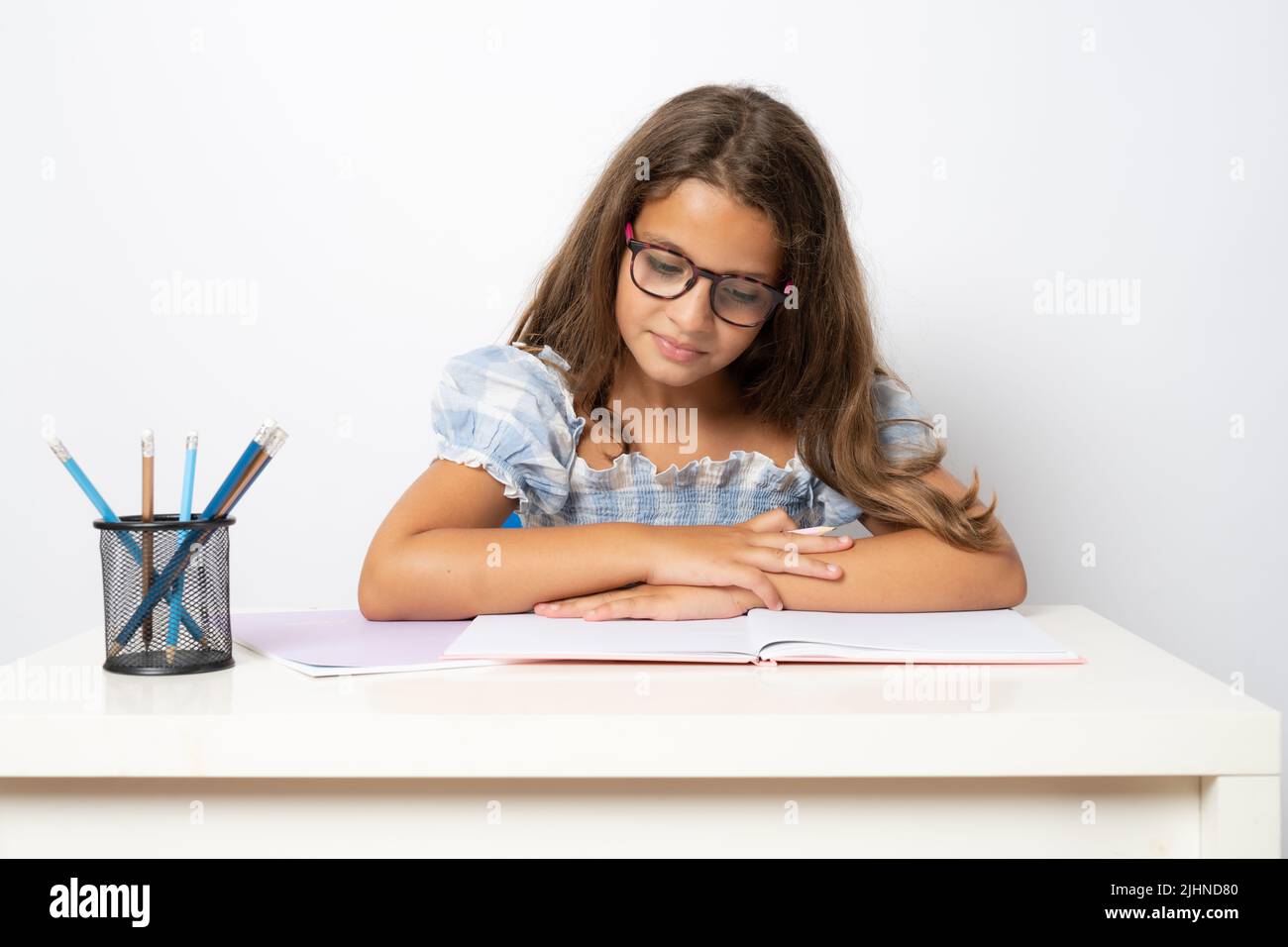 Portrait of positive school girl sitting behind desk reading a book ...