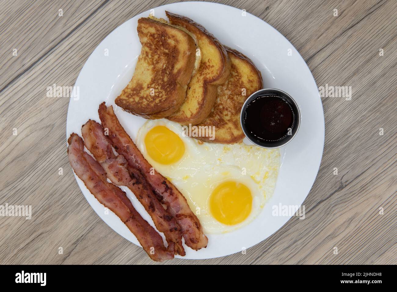 Overhead view of traditional American breakfast consisting of french toast, fried eggs, and bacon will ensure that the belly will be full. Stock Photo