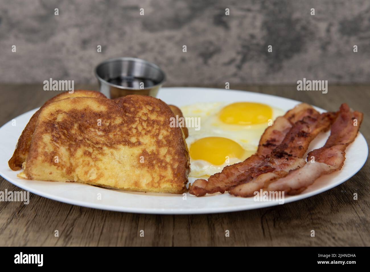 Traditional American breakfast consisting of french toast, fried eggs, and bacon will ensure that the belly will be full. Stock Photo