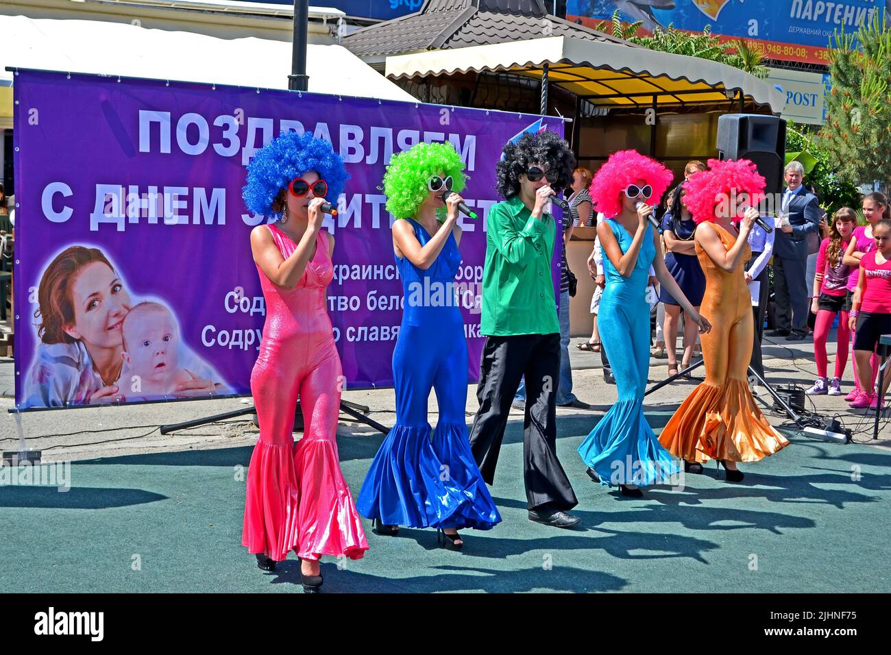 Concert at embankment devoted to Children Protection Day. Music singers in rainbow periwigs and tight dress singing. Stock Photo