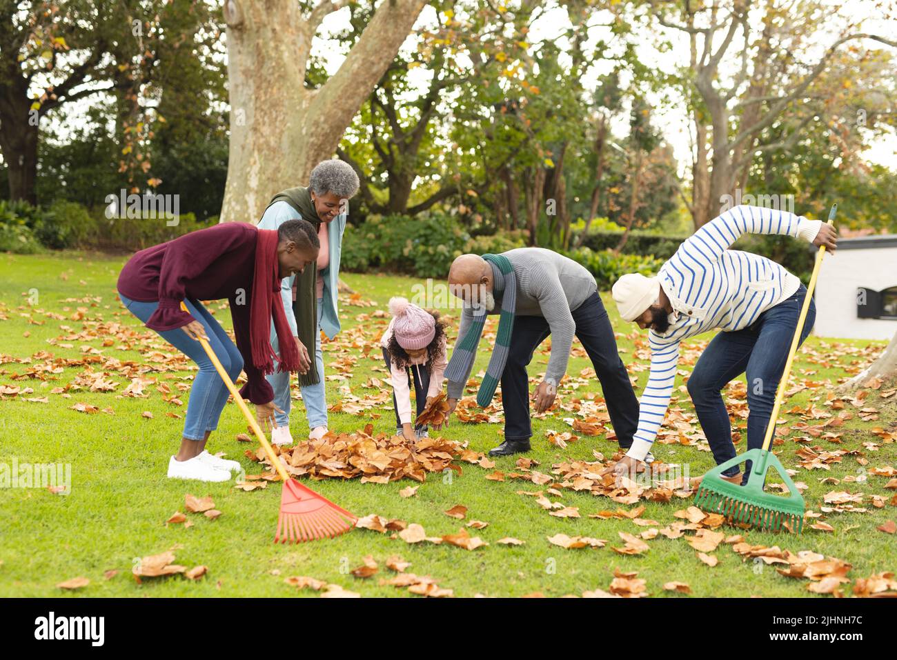 Image of happy african american multi generation family swiping leaves in autumn garden Stock Photo