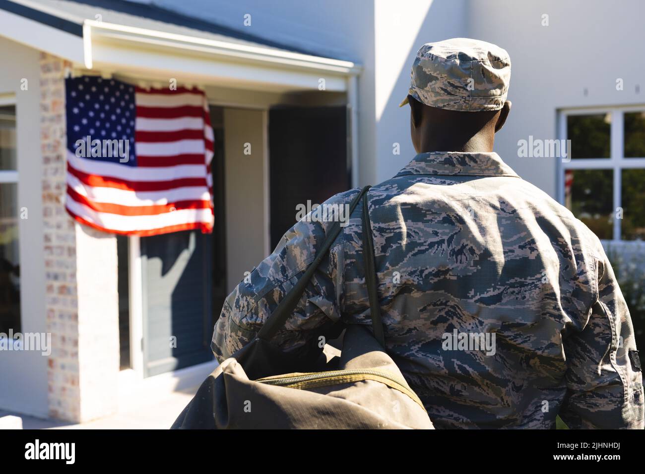 Rear view of army soldier in camouflage clothing with backpack standing outside house in yard Stock Photo