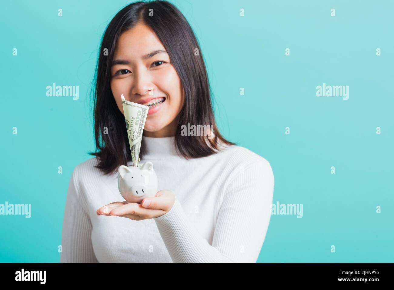 Asian beautiful young woman holding piggy bank on hands and putting ...