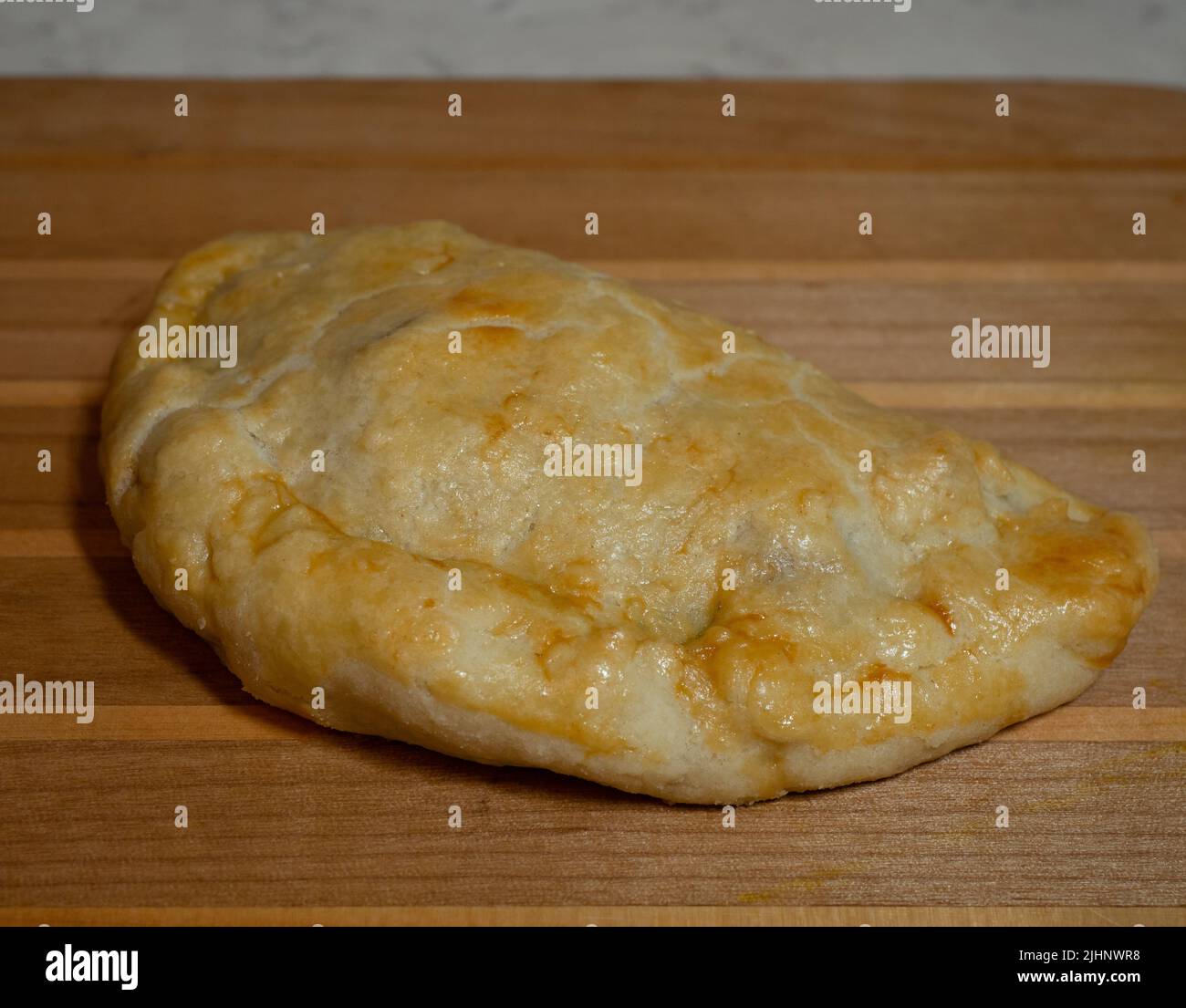 Single golden brown pasty on a wooden cutting board. Stock Photo