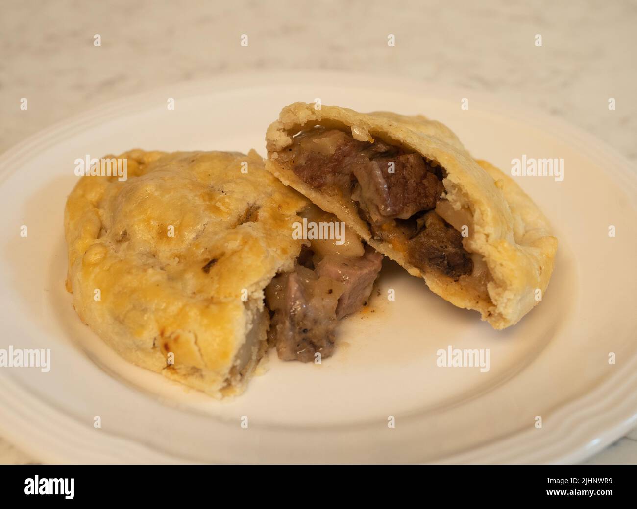 Pasty cut open with beef filling on a white plate. Stock Photo