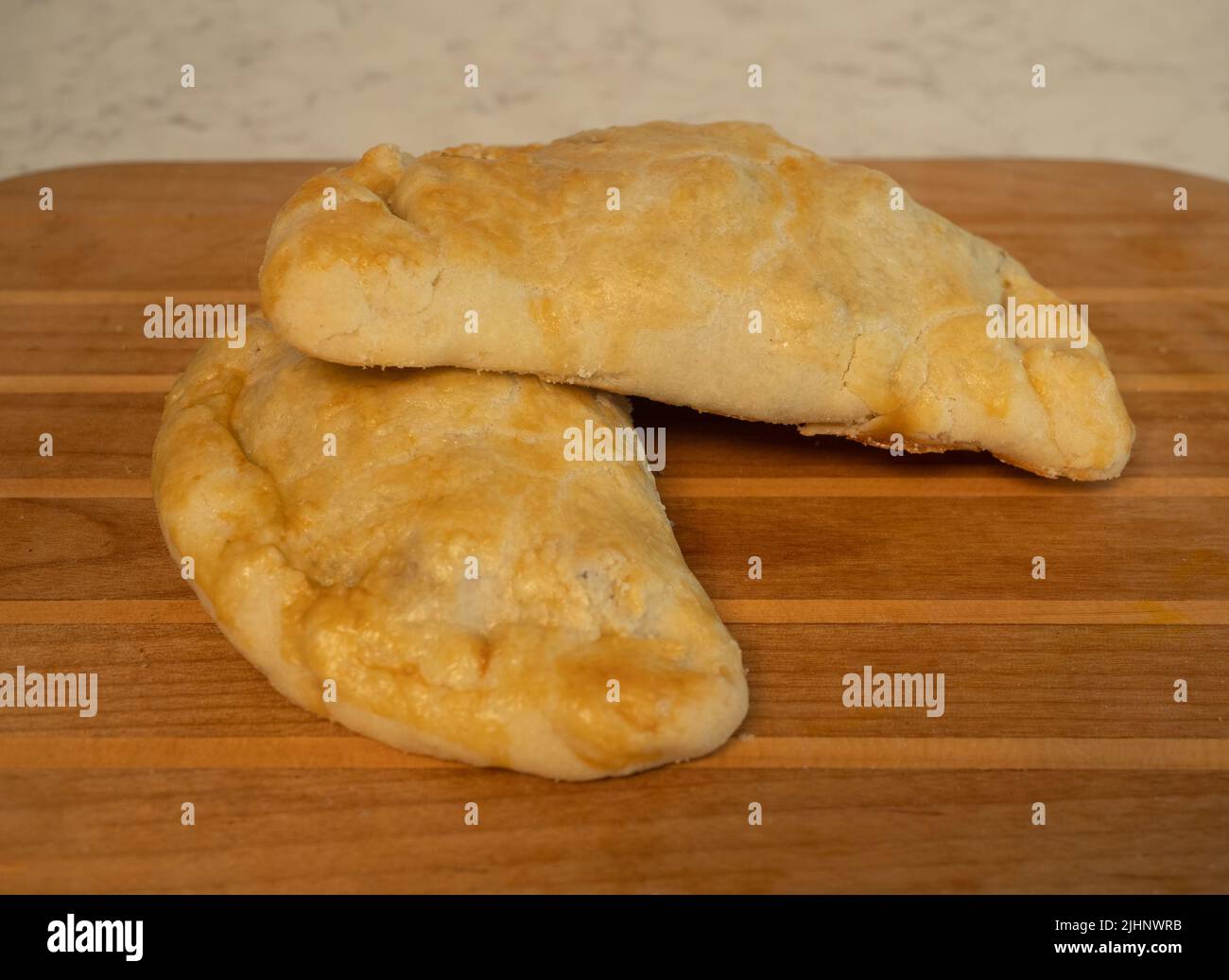 Two fresh baked beef and potato pasties on a wooden cutting board. Stock Photo