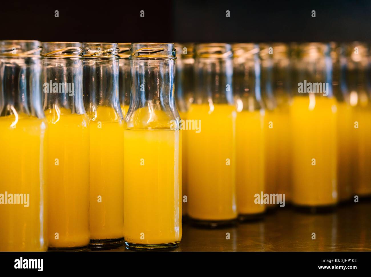 Close up group of fresh pineapple juice in small glass bottles, cold fresh pineapple juice in glass container on stainless steel shelf. Stock Photo