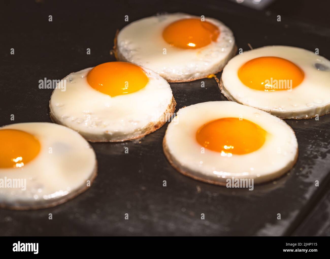 Row of fried egg on black griddle with warm lighting in a restaurant. Stock Photo