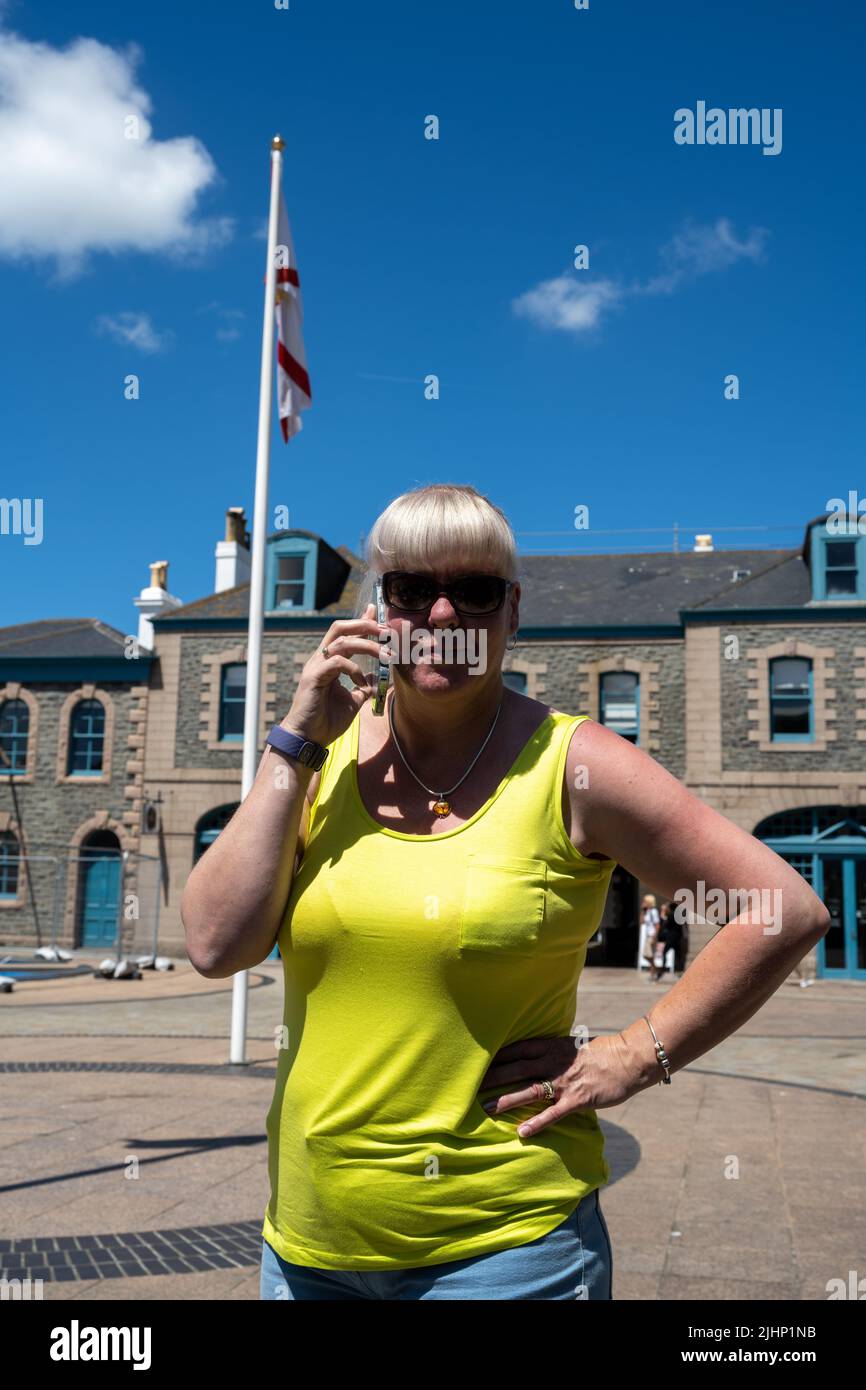 Mature female tourist wearing sunglasses and a yellow top on a mobile phone whilst on holiday in summer. Stock Photo
