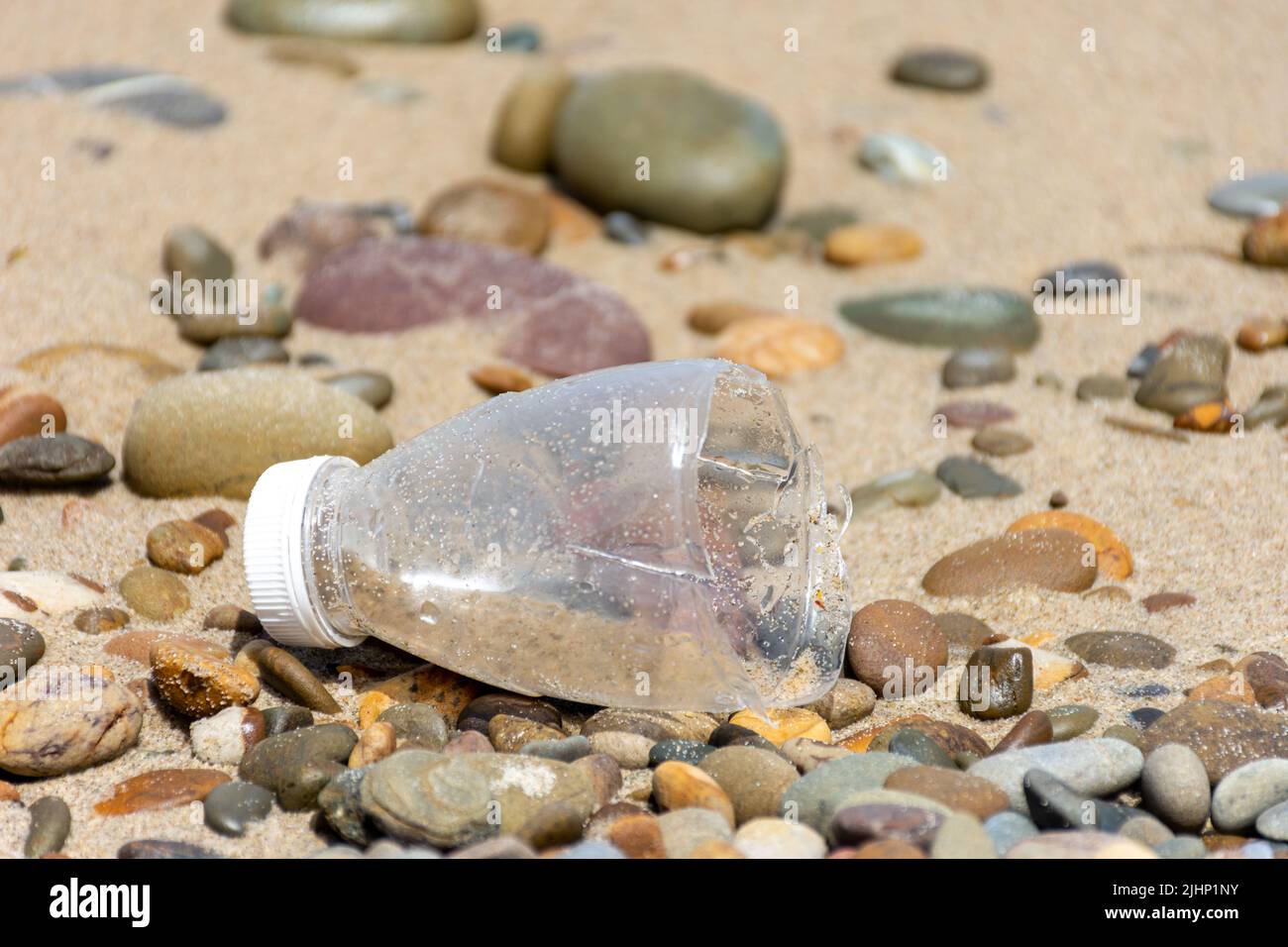 Half plastic bottle on a pebble beach. Save planet concept. Stock Photo