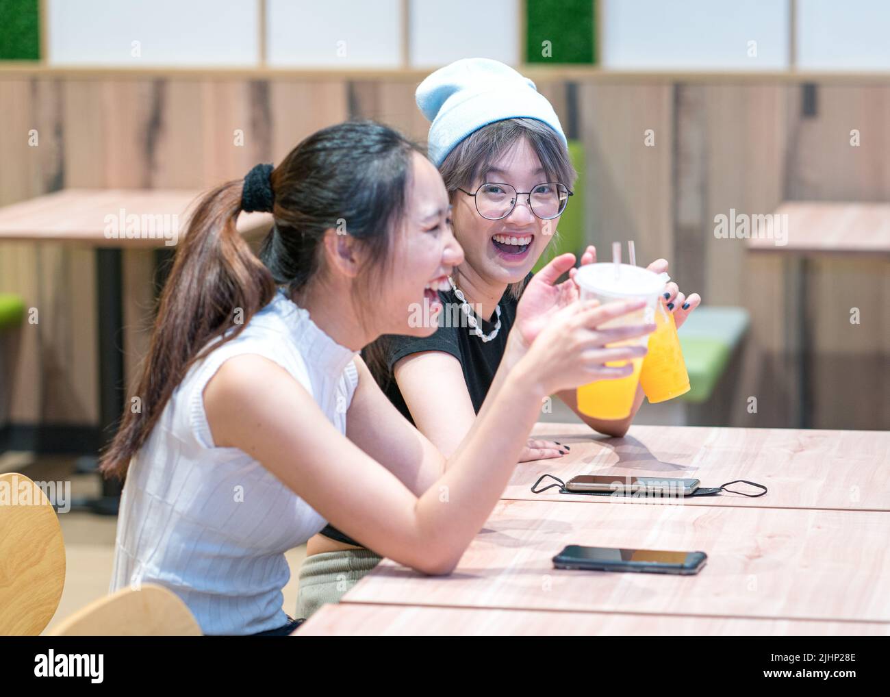 Two girlfriends, Asian ethnicity having a good laugh and a drink in a restaurant. Stock Photo