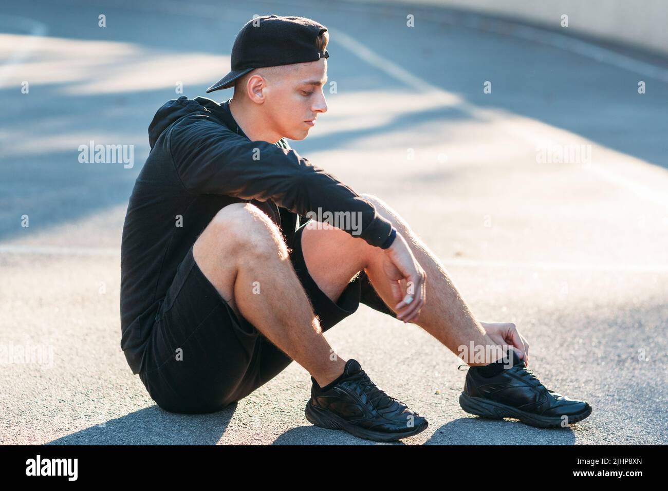 Young sporty man sitting on ground at stadium Stock Photo - Alamy