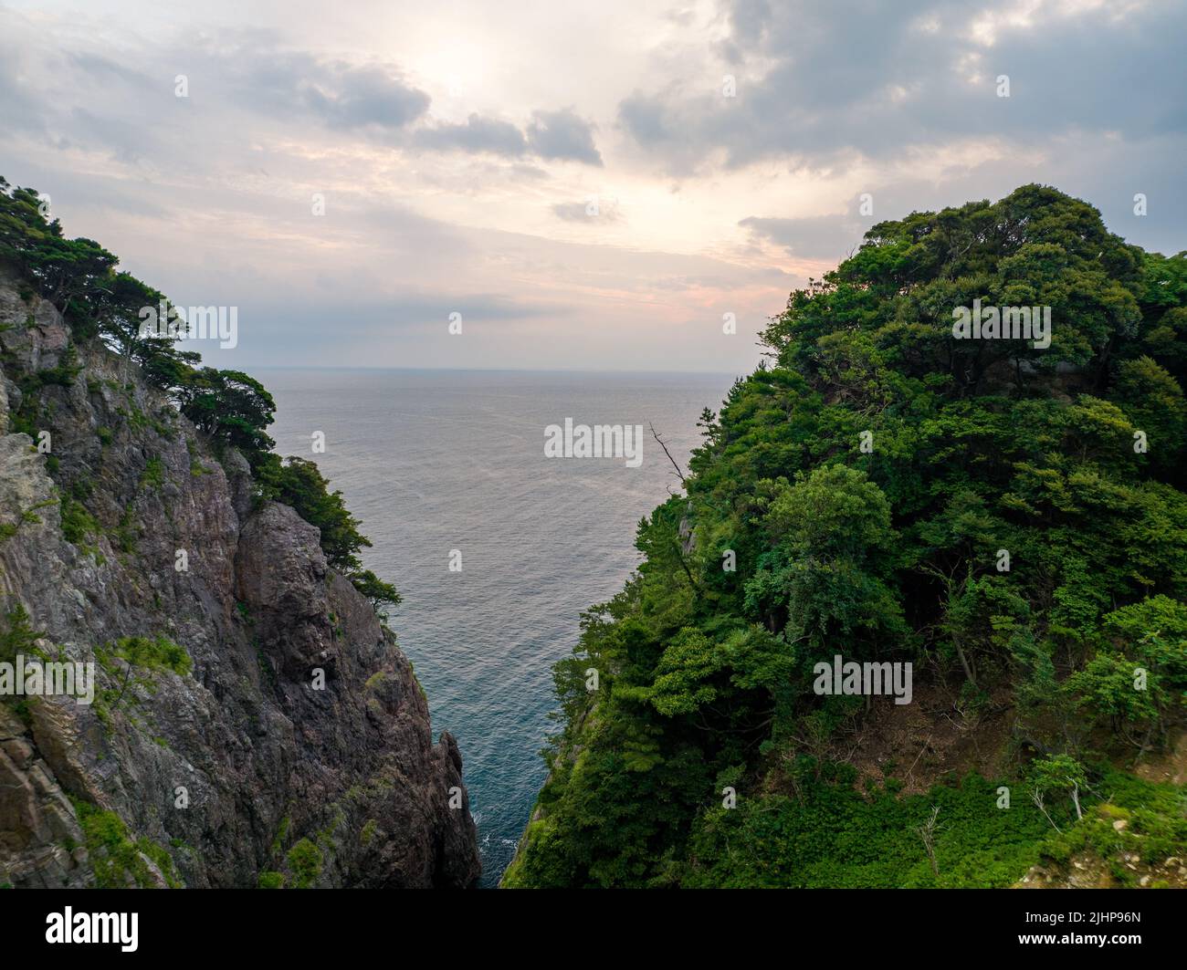 Opening between rugged coastal cliffs reveals morning sunrise on calm sea Stock Photo