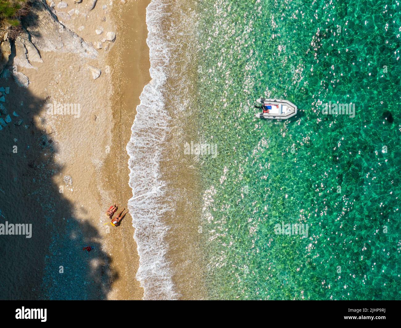 Aerial view of a moored dinghy floating on a transparent sea. Beach and
