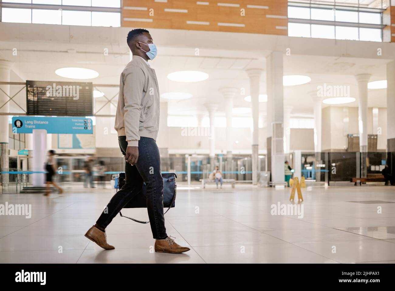 African american businessman travelling alone and walking in a train station while wearing a mask for protection against coronavirus. Young black male Stock Photo