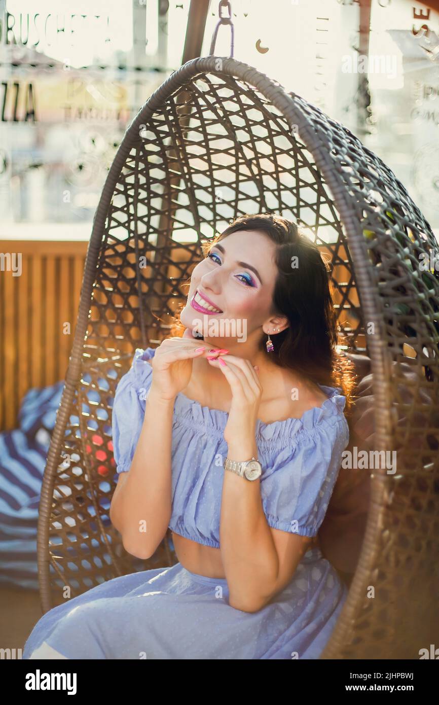 A beautiful young woman is sitting in a wicker hanging chair on the ...