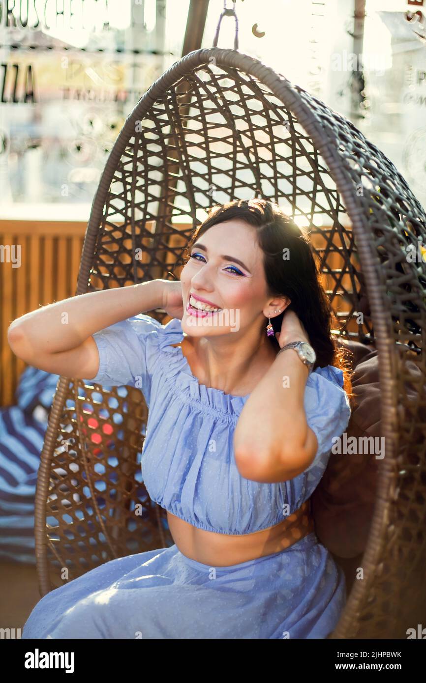 A beautiful young woman is sitting in a wicker hanging chair on the ...