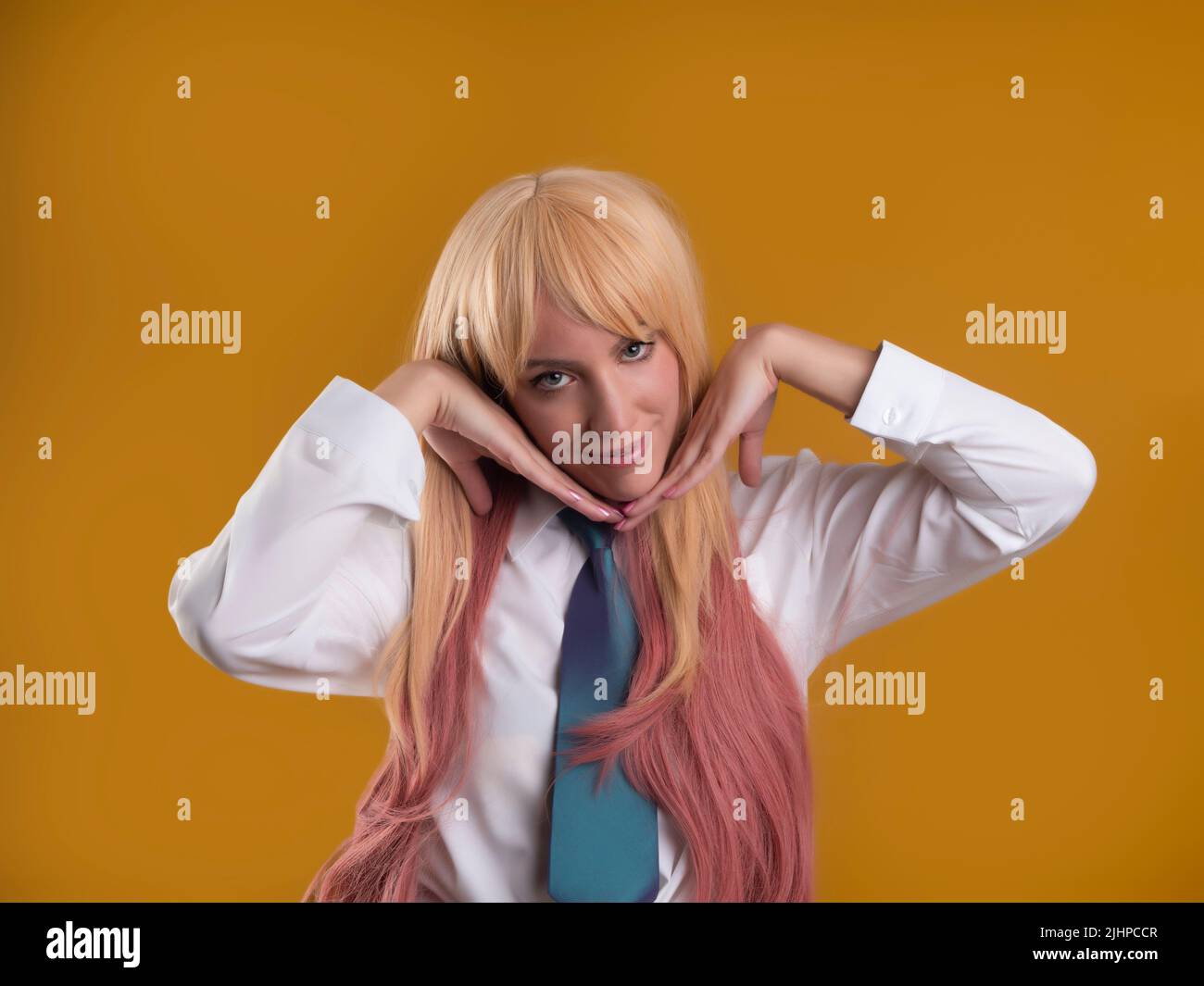 Charming female model with pink hair in white shirt and tie looking at camera with hands under chin on brown background in studio Stock Photo