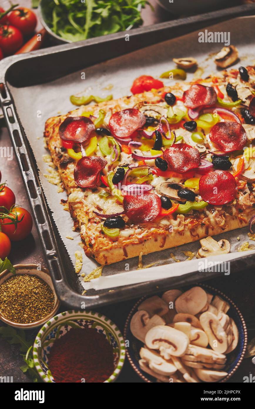 A piece of square pizza with basil pepperoni tomatoes and mushrooms on a iron tray Stock Photo