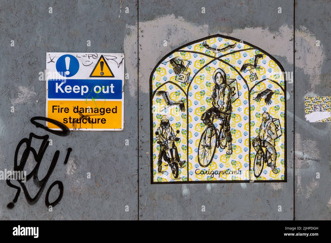 Graffiti depicting food delivery riders and herons on the hoarding covering the burnt out building that used to be Mr Gees on Mill Rd, Cambridge. Stock Photo