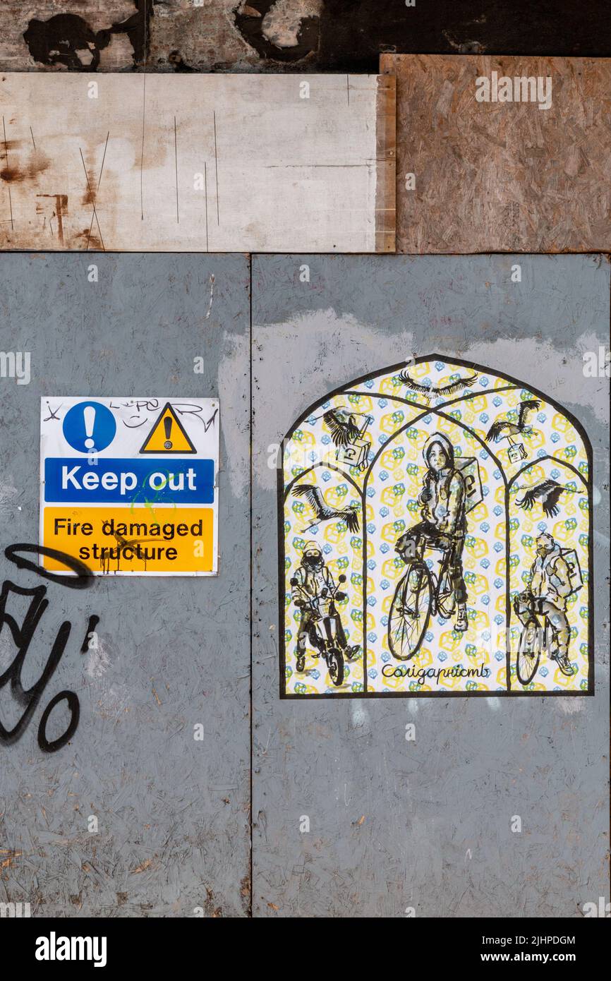 Graffiti depicting food delivery riders and herons on the hoarding covering the burnt out building that used to be Mr Gees on Mill Rd, Cambridge. Stock Photo