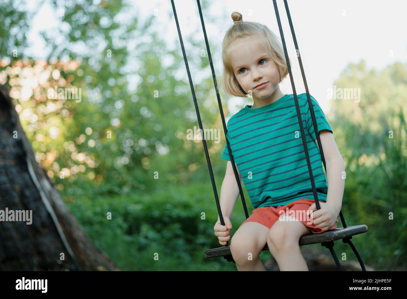 Adorable little boy with long blond hair swings on a fresh air on a