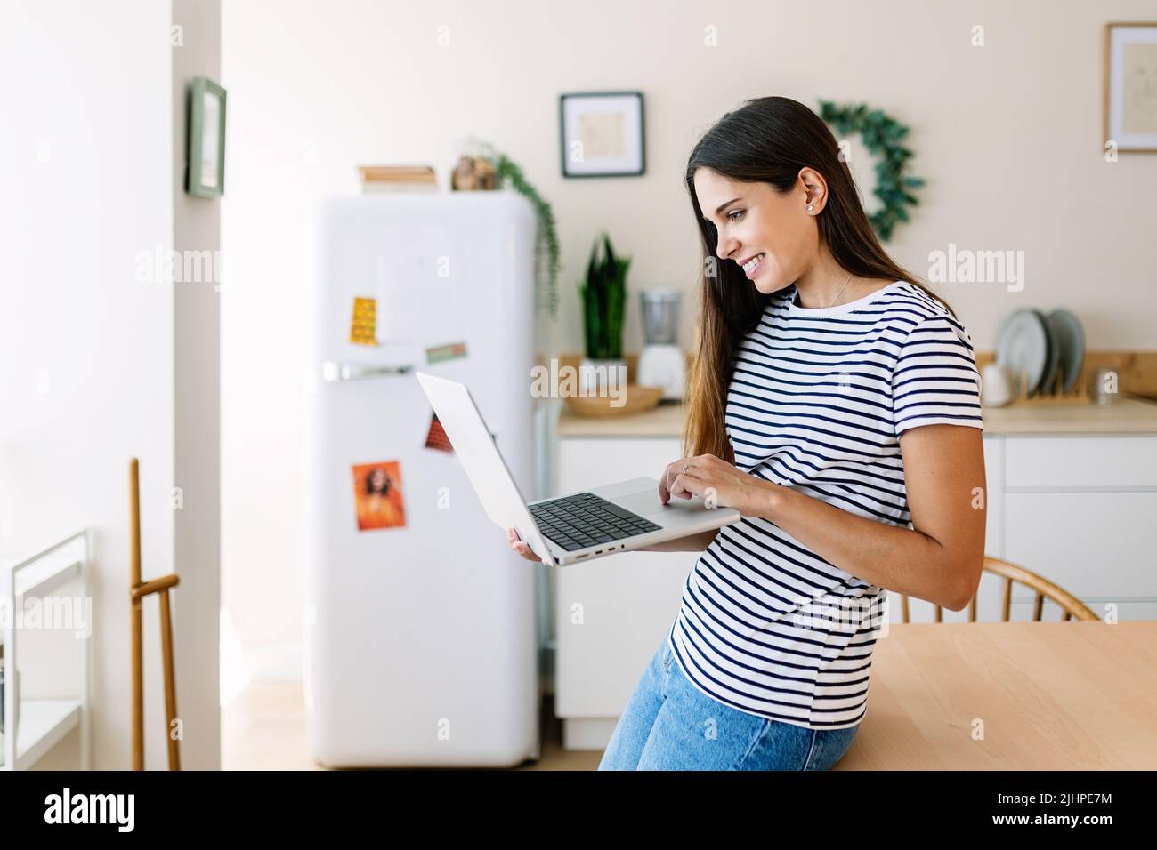 Smiling young caucasian woman typing on laptop while working from home Stock Photo